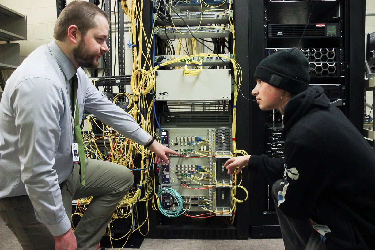 Instructor with student in front of computer hardware